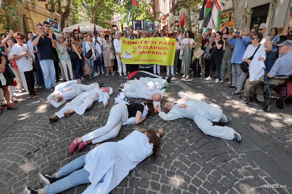Flash mob per Gaza a Napoli: attivisti distesi a terra simulano le vittime dei bombardamenti, mentre il pubblico osserva con bandiere e striscioni