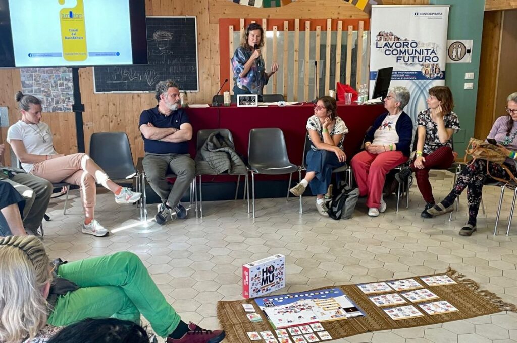 Workshop al convegno sull’abitare collaborativo presso il cohousing Case Franche, con partecipanti seduti in cerchio attorno al gioco cooperativo Ho-Mu.