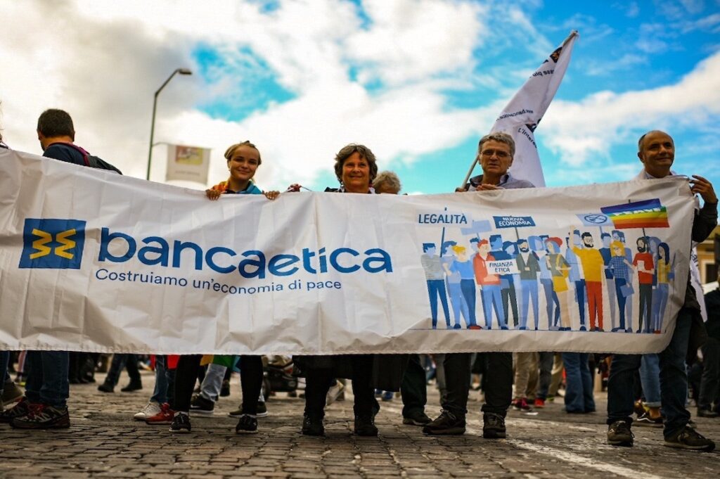 Persone socie e clienti di Banca Etica alla marcia della pace Perugia-Assisi 2025, con uno striscione dedicato alla finanza etica