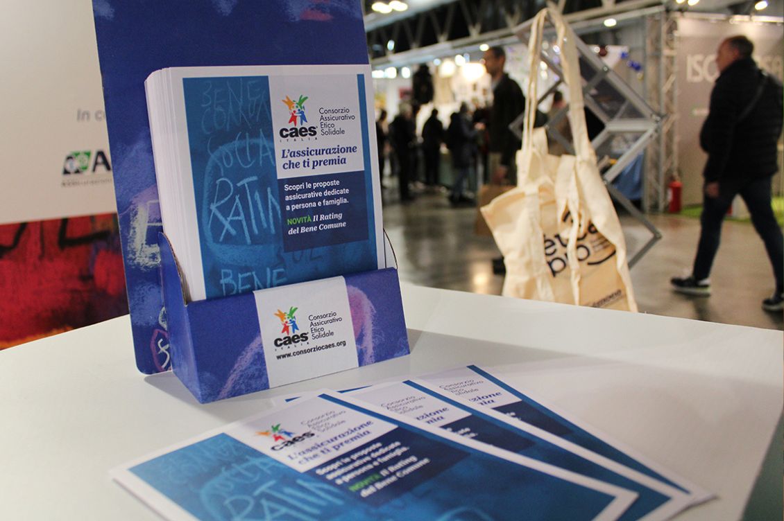 Materiale informativo del Consorzio CAES in esposizione a un evento fieristico, con depliant sull’assicurazione etica
