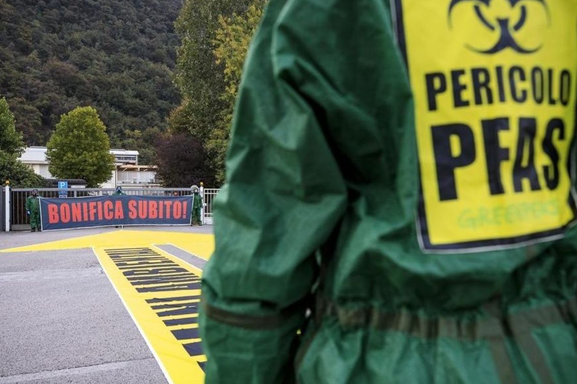 Attivista Greenpeace con tuta anti-contaminazione durante una protesta davanti alla fabbrica Miteni, con striscione “Bonifica subito”