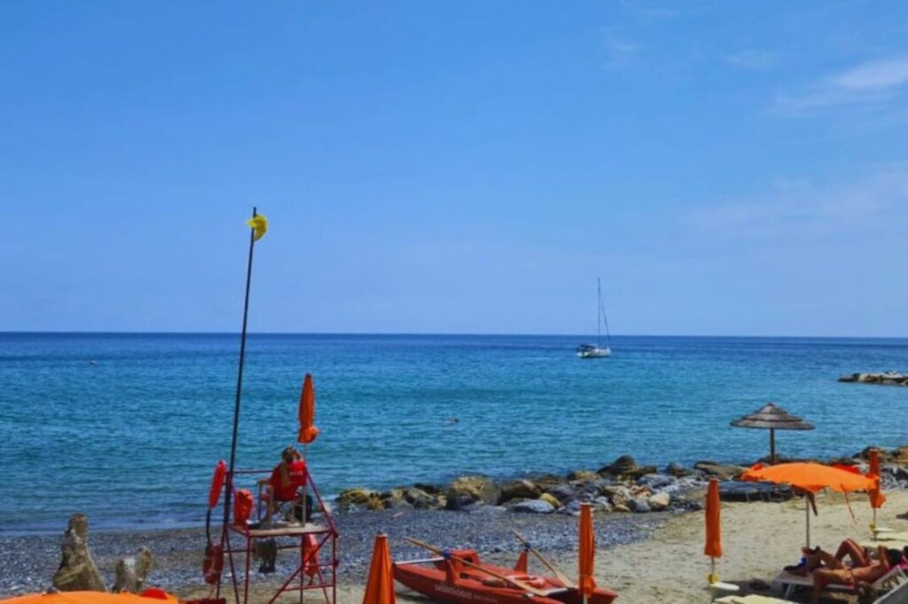 Vacanza olistica a Albenga: una spiaggia tranquilla con ombrelloni arancioni e mare cristallino, tra i luoghi vissuti dai partecipanti delle Vacanze Nonsolomare.