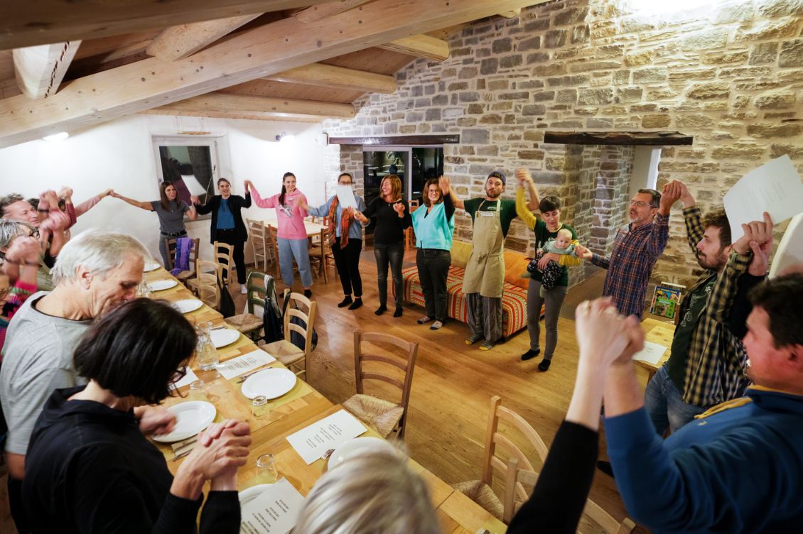 Partecipanti al Capodanno detox ad Autosufficienza riuniti in cerchio prima della cena, in una sala rustica in pietra e legno sull’Appennino romagnolo.