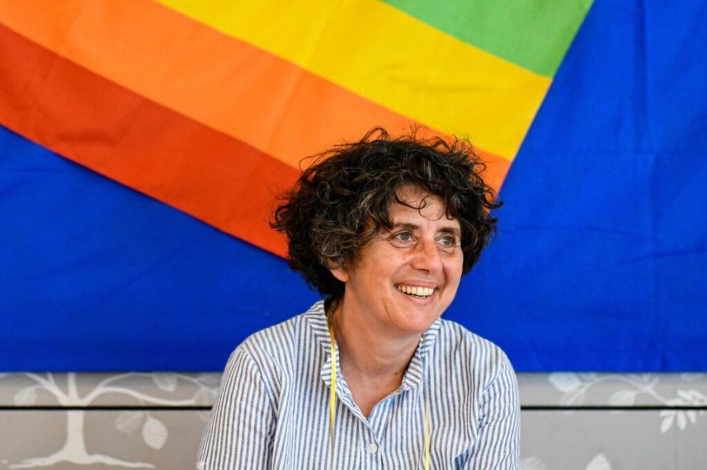 Teresa Masciopinto sorride davanti a una bandiera arcobaleno durante un incontro legato a Banca Etica