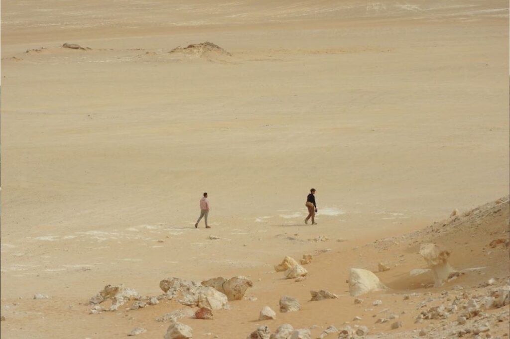 Due persone camminano nel deserto egiziano tra rocce e sabbia durante un viaggio di turismo responsabile