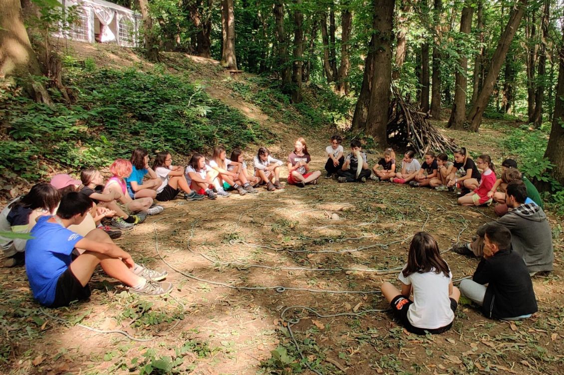 Ragazzi e ragazze in cerchio nel bosco durante i campi estivi di Liberi Sogni a Cascina Rapello